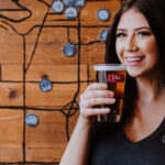 photo of a female CRAFT employee holding up a pint of beer